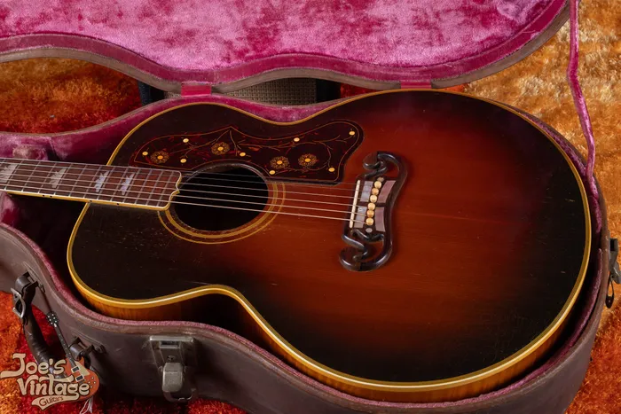 A 1948 Gibson SJ-200 sunburst acoustic guitar in its original-style case, showing the flower pickguard, crown inlays, and open moustache bridge.