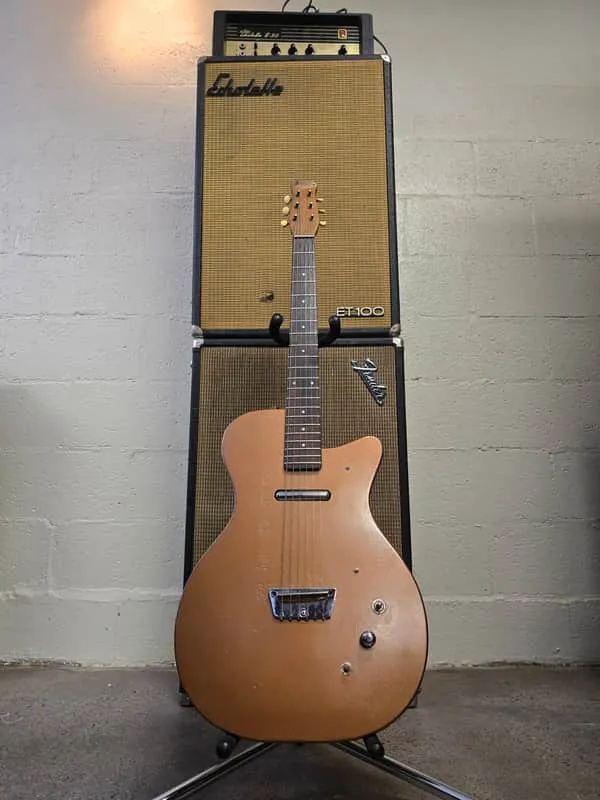 Bronze refinished 1950s Danelectro U-1 with a single lipstick pickup, standing in front of amplifiers.