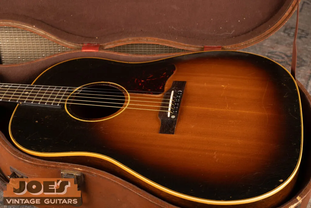 A vintage 1950s Gibson J-45 “Workhorse” acoustic guitar with a sunburst finish and original teardrop pickguard resting in its case at Joe’s Vintage Guitars