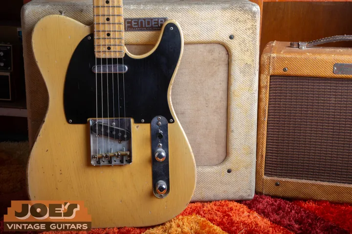 Blonde Telecaster with a black pickguard in front of tweed Fender amplifiers
