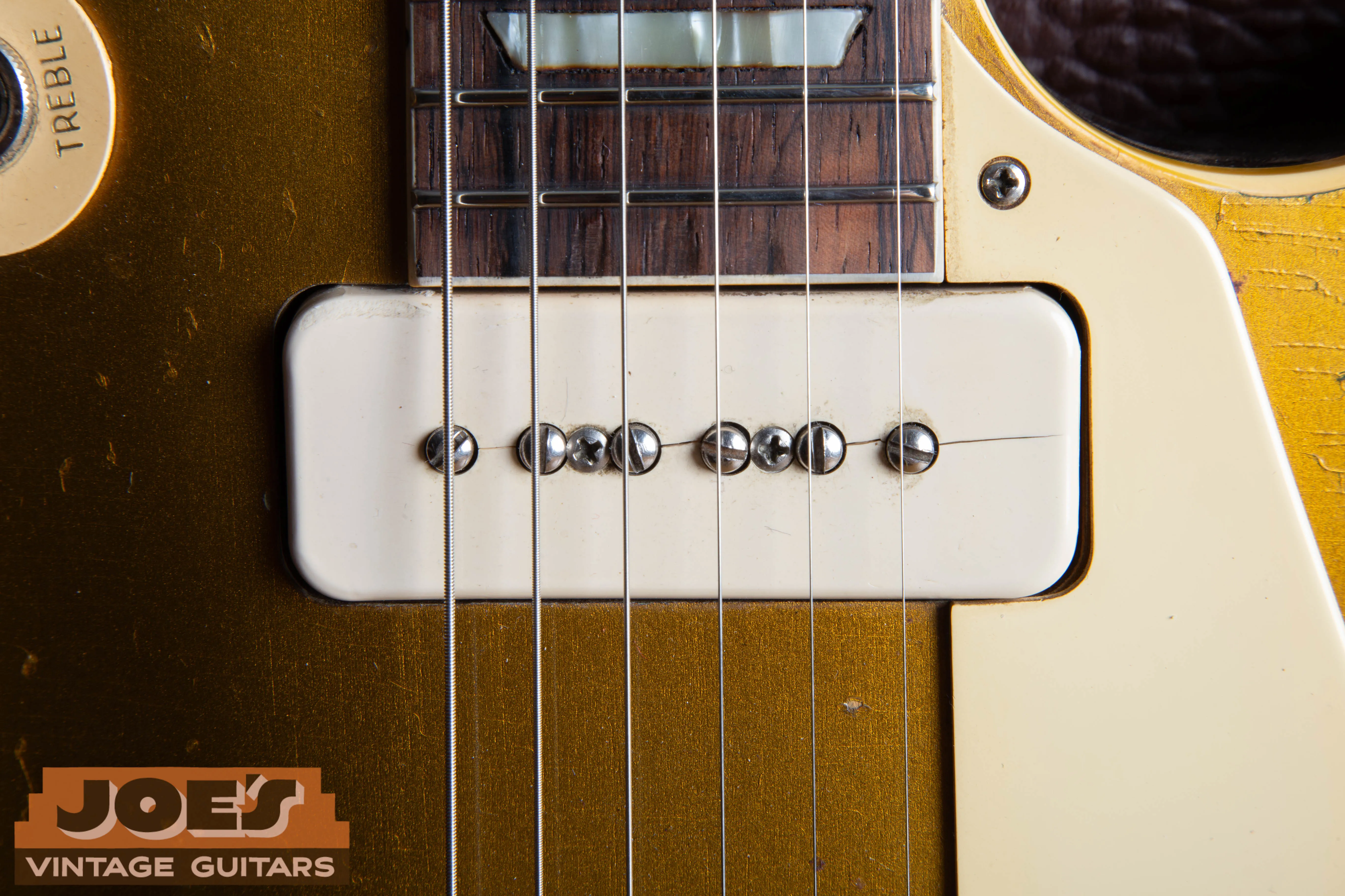 Macro close-up of a 1956 Gibson Les Paul neck P-90 pickup showing a cream Royalite soapbar cover with a vintage hairline split running along the center of the pole pieces.