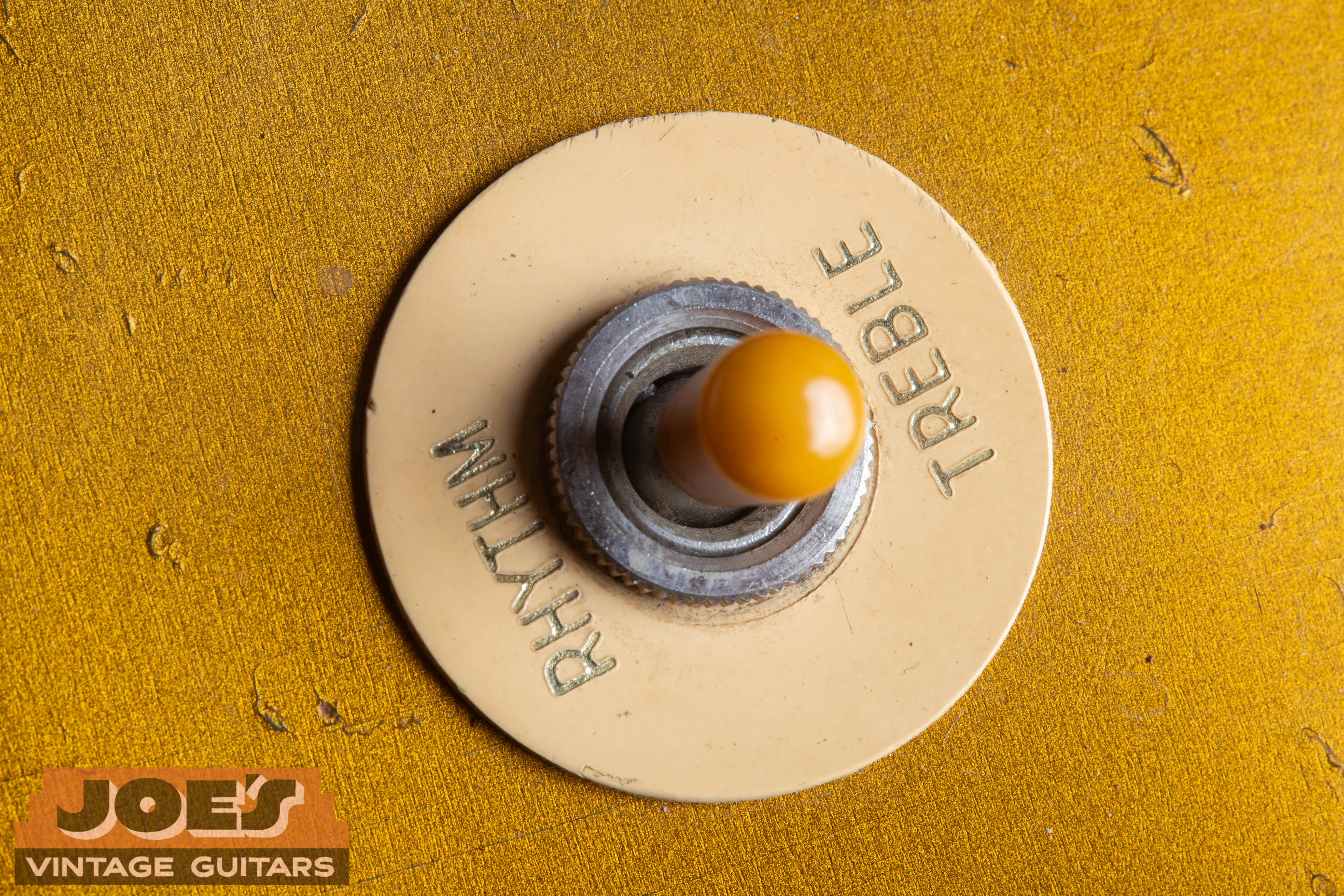 Close-up of a 1956 Gibson Les Paul 3-way toggle switch featuring an aged amber Catalin tip and a cream “poker chip” selector ring with gold-embossed lettering.
