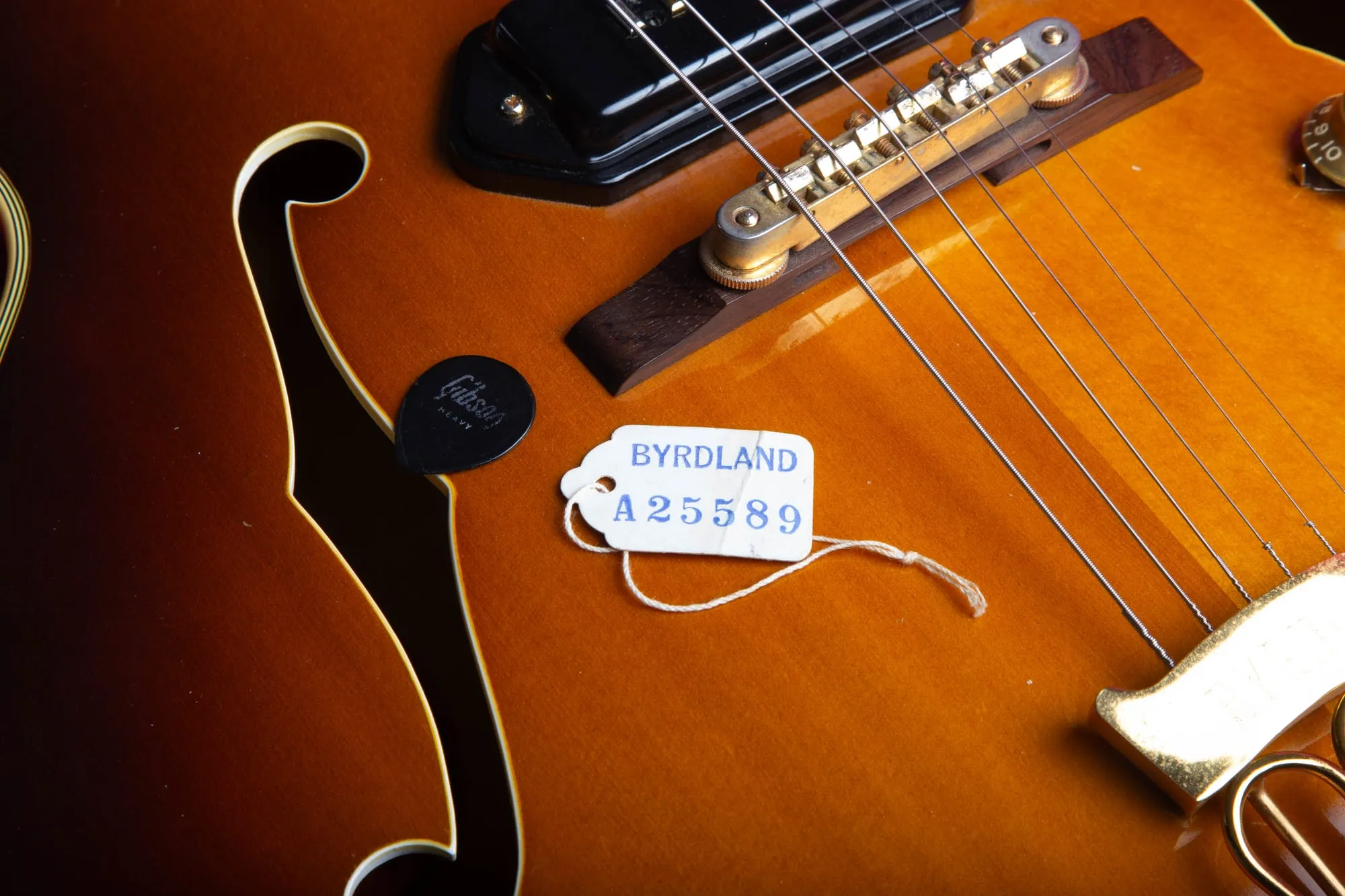 Old paper hang tag on a 1957 Gibson Byrdland stamped BYRDLAND A25589, resting on the sunburst top near the bridge