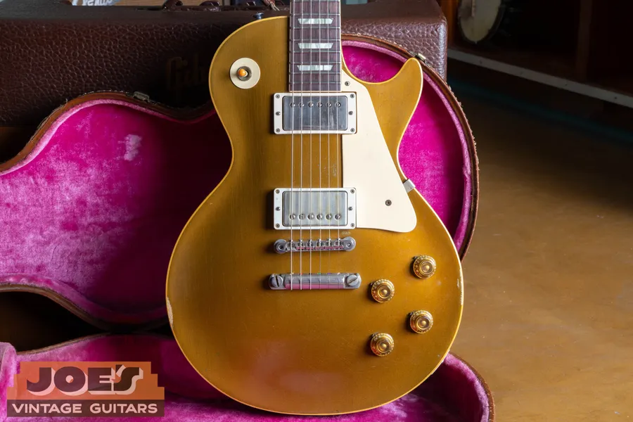 Goldtop Les Paul with two covered pickups and a cream pickguard beside a pink-lined case