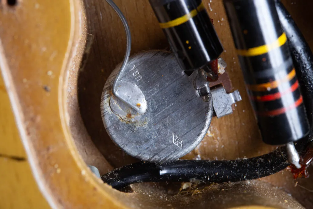 Close-up of an original 1958 Centralab (CRL) potentiometer inside a Gibson Les Paul Special control cavity. The metal casing clearly shows the stamped “USA” text and the small characteristic diamond CRL logo. The component is wired with original period-correct solder and a Bumblebee capacitor, set against the mahogany wood grain of the internal routing.