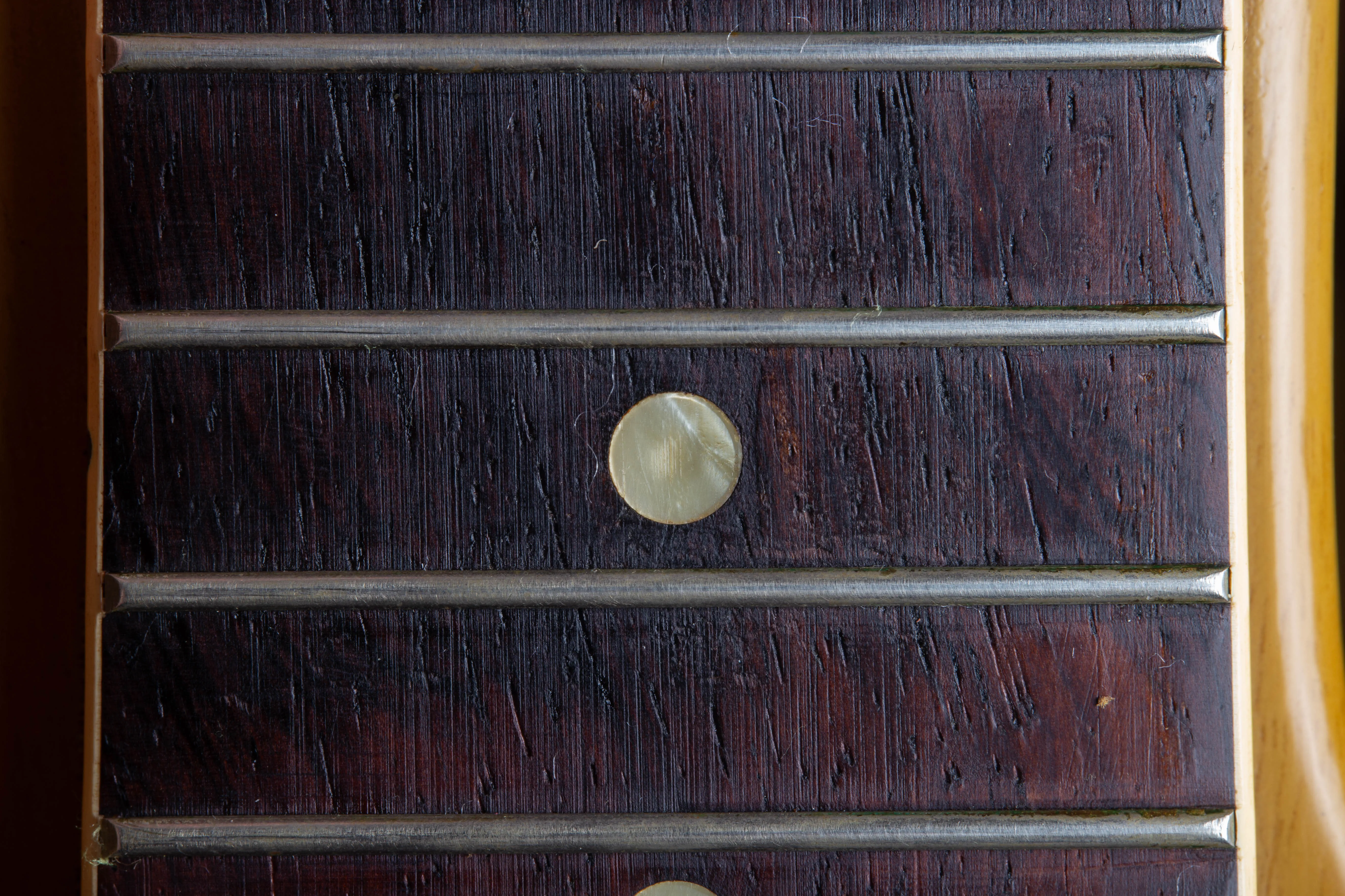 A detailed perspective of an original 1958 Gibson Les Paul Special fretboard dot inlay. The image captures the organic, “wavy” texture of the mother-of-pearl material, showcasing a distinct iridescent shimmer and subtle greenish-grey tinting caused by decades of natural aging on the dark rosewood fingerboard.