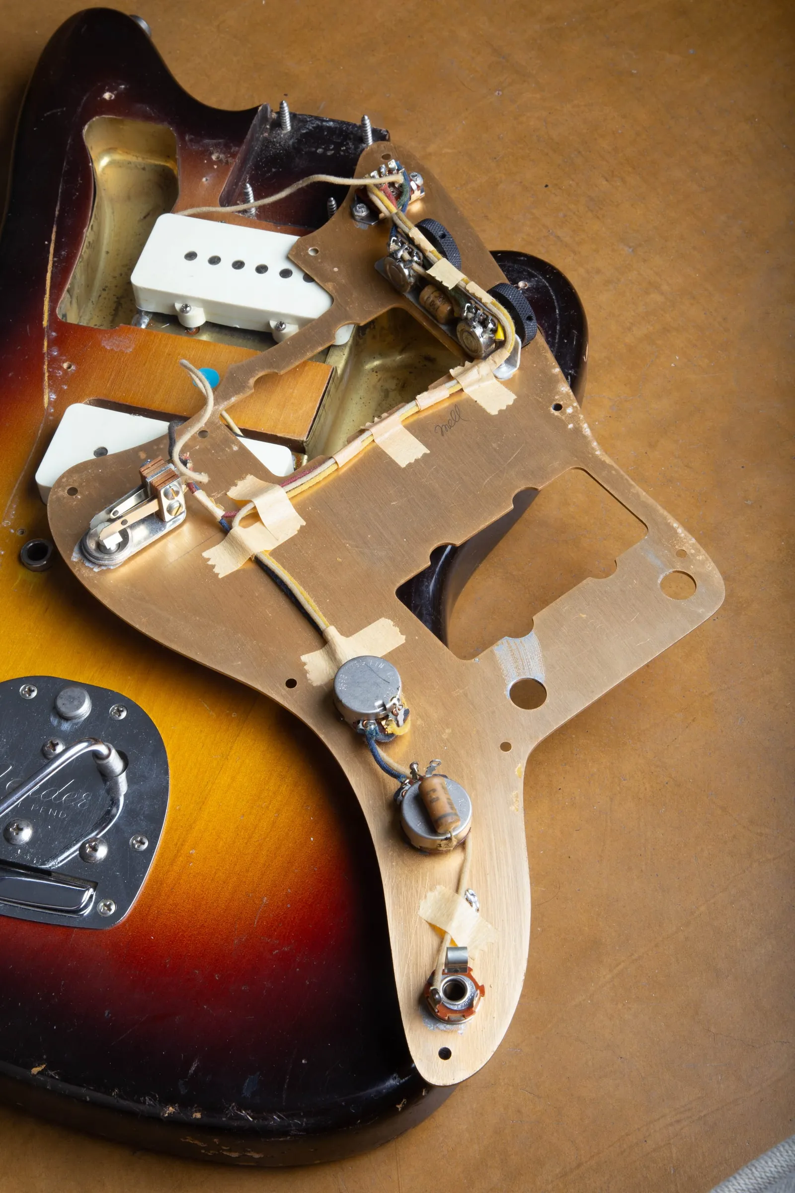 The underside of a 1959 Fender Jazzmaster gold anodized guard lifted from the body, showing the shielding plate and the rhythm circuit assembly with cloth wiring