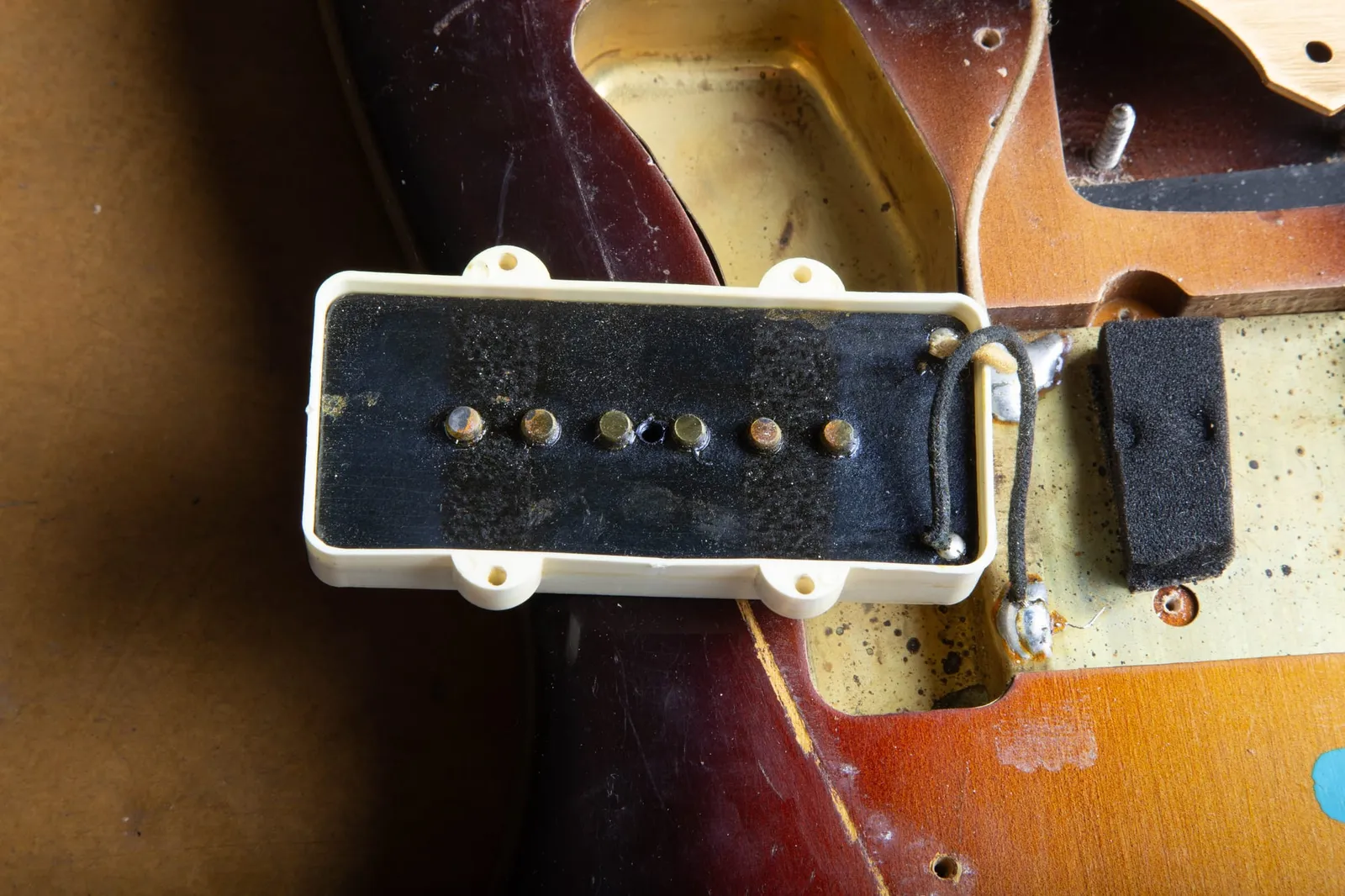 The underside of a 1959 Fender Jazzmaster neck pickup showing black fiber flatwork, six pole pieces, cloth lead wire, and the original height-adjustment foam