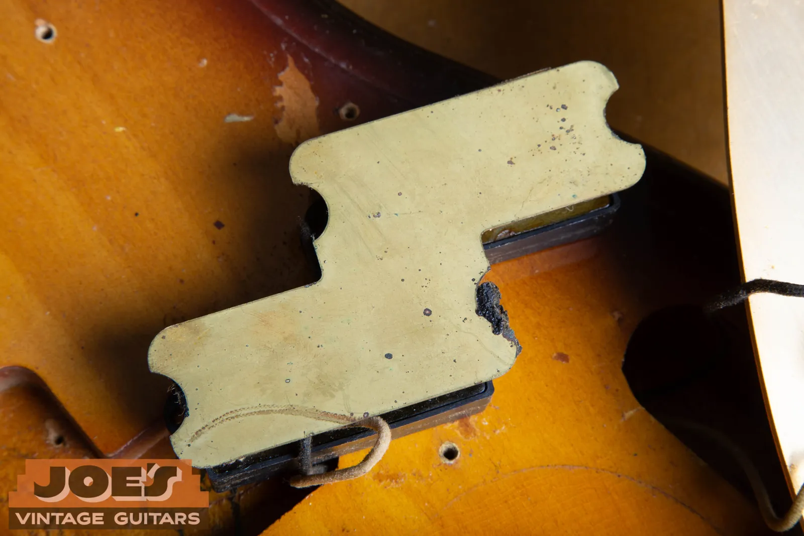 The gold anodized aluminum pickup mounting plate lifted from the body of a 1959 Fender Precision Bass, with the split coil pickup underneath it