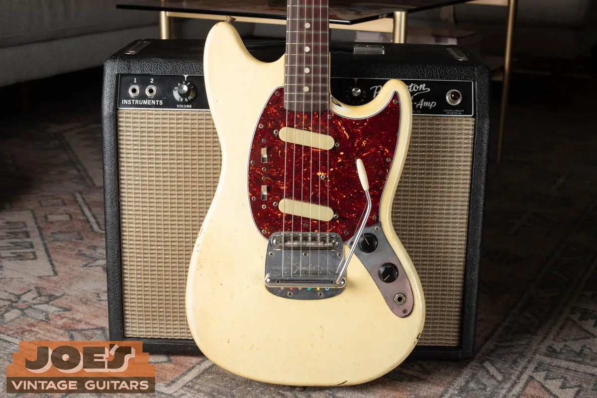 Early 1960s Fender Mustang in Olympic White with a tortoiseshell celluloid pickguard leaning against a vintage Fender amplifier