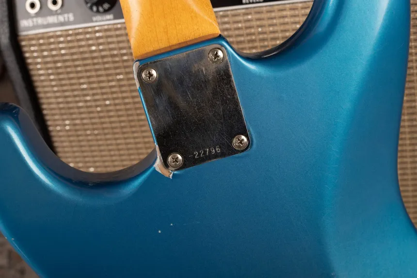 Neck plate on a refinished blue metallic Fender Stratocaster, with ridged finish and a chip showing grey primer.