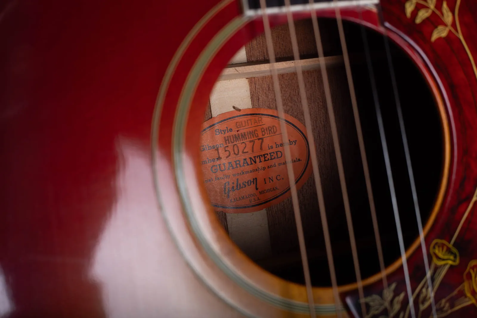 Orange oval Gibson label seen through the soundhole of a mid 1960s Hummingbird, reading Style Guitar Humming Bird, number 150277, Gibson Inc, Kalamazoo Michigan.