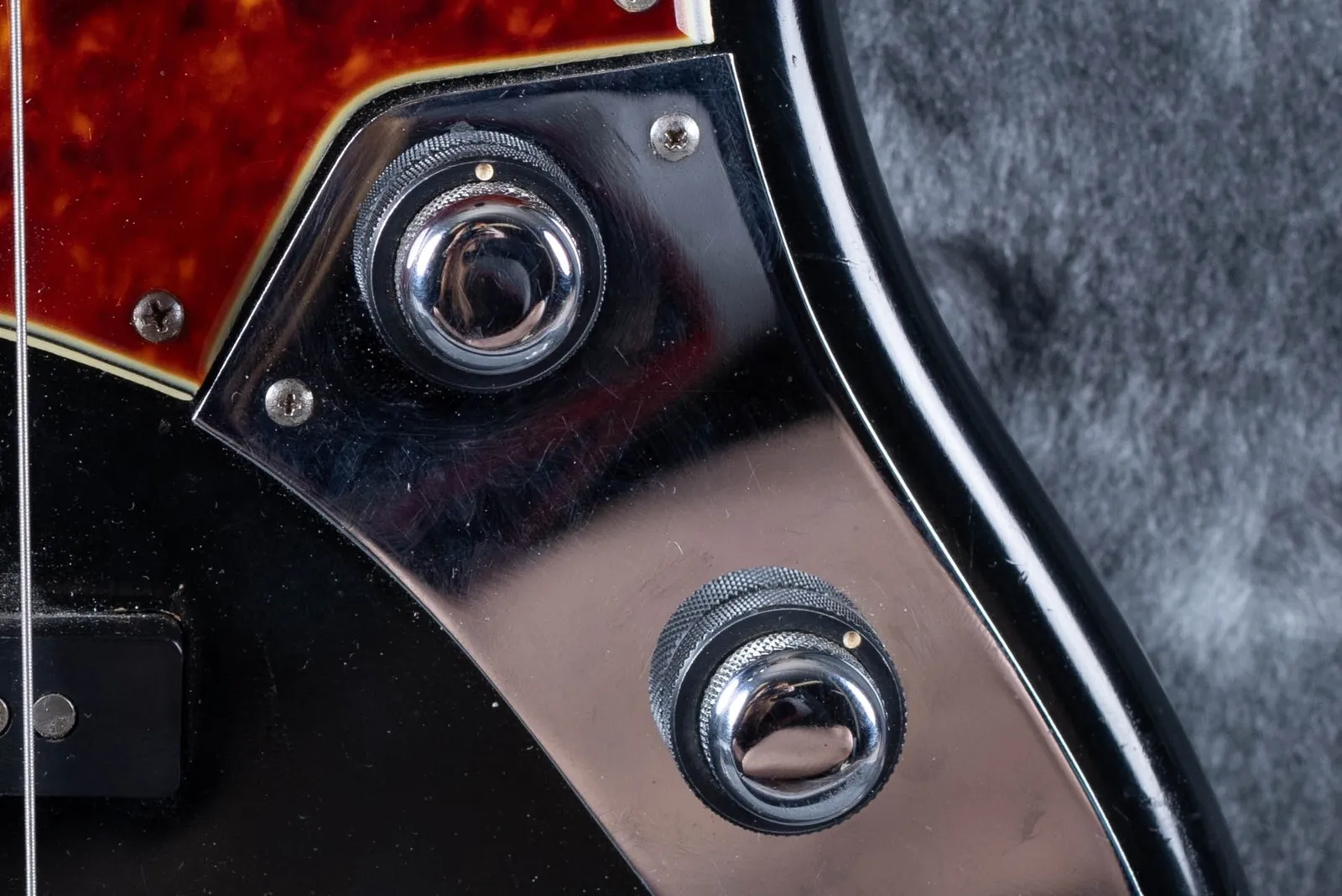Close up of the chrome control plate on a 1961 Fender Jazz Bass showing two stacked concentric knobs, each a volume and tone pair