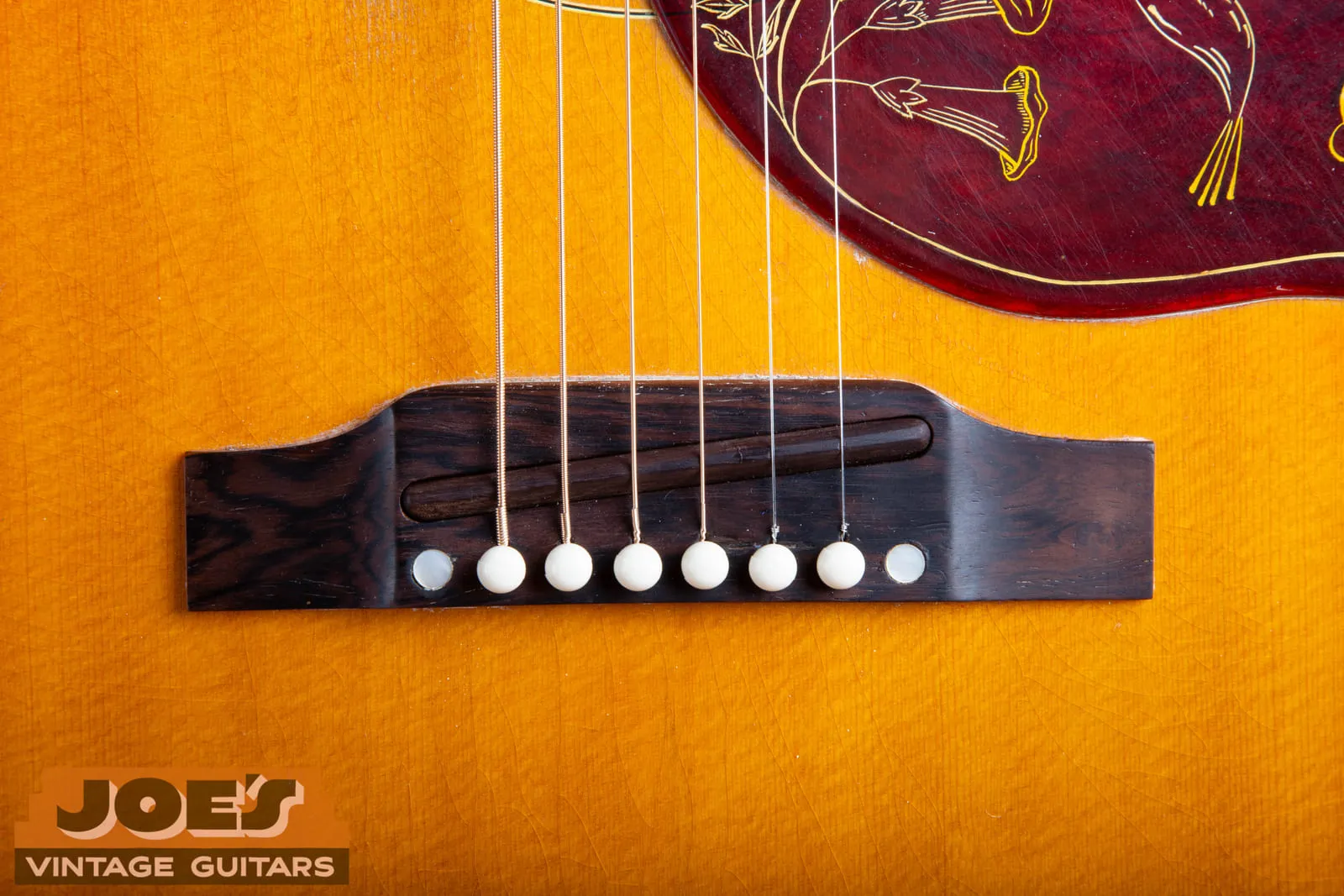 Close up of the rectangular rosewood bridge on a 1961 Gibson Hummingbird, showing a rosewood saddle set into the routed slot with no height adjustment screws present.