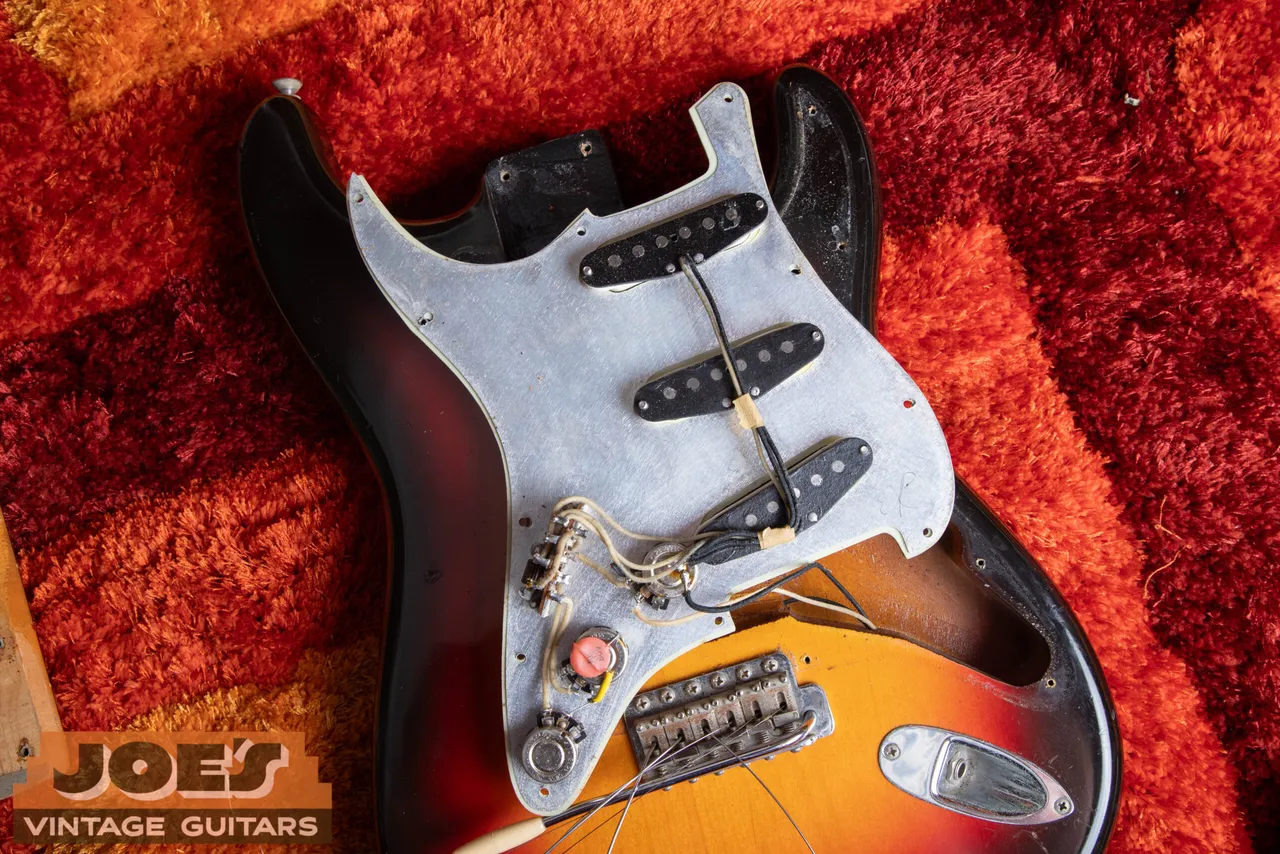 The three black-bottom pickups under the pickguard of a 1962 Fender Stratocaster with cloth-covered wiring