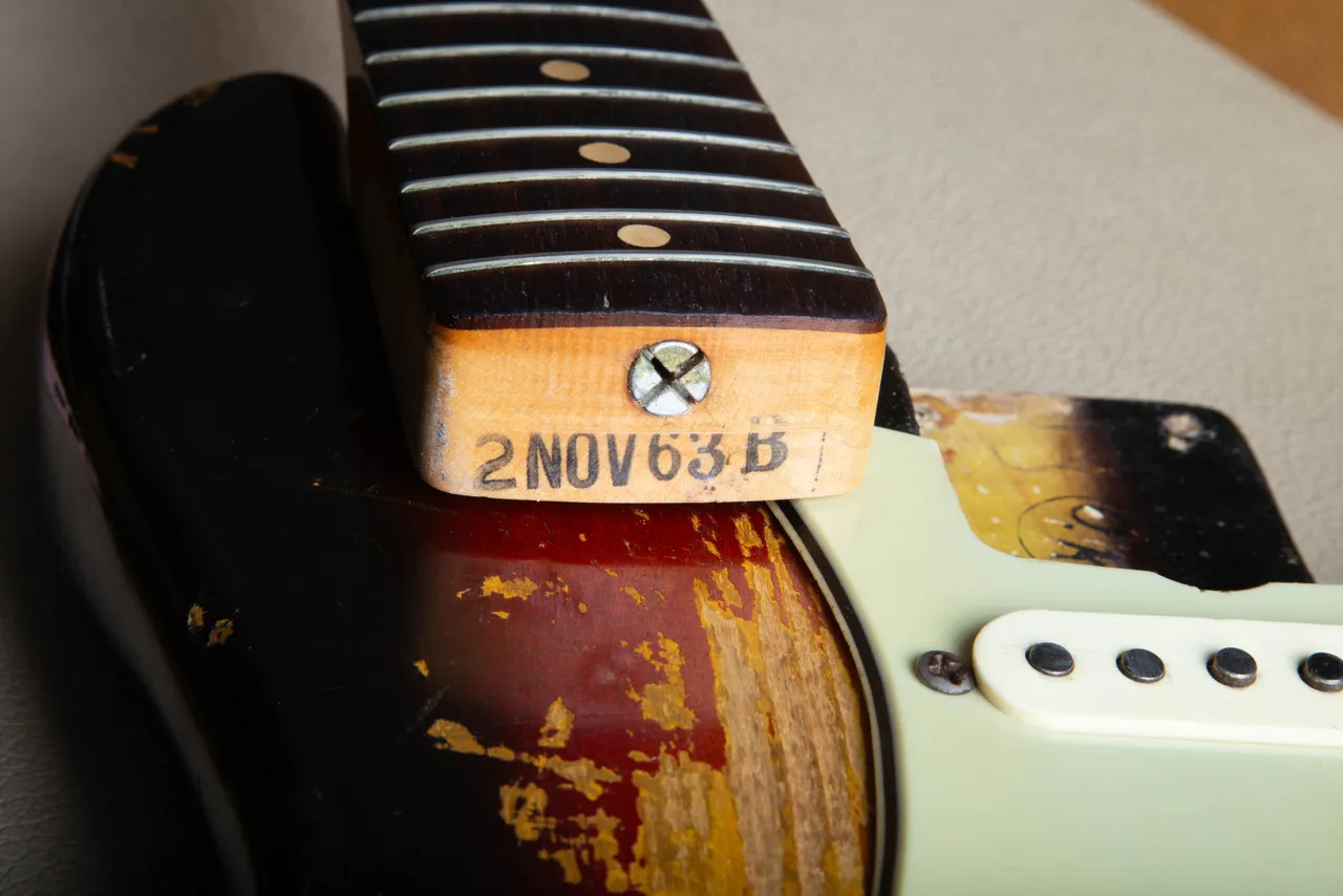 Ink stamp on the exposed wooden end of a detached guitar neck during specialist inspection
