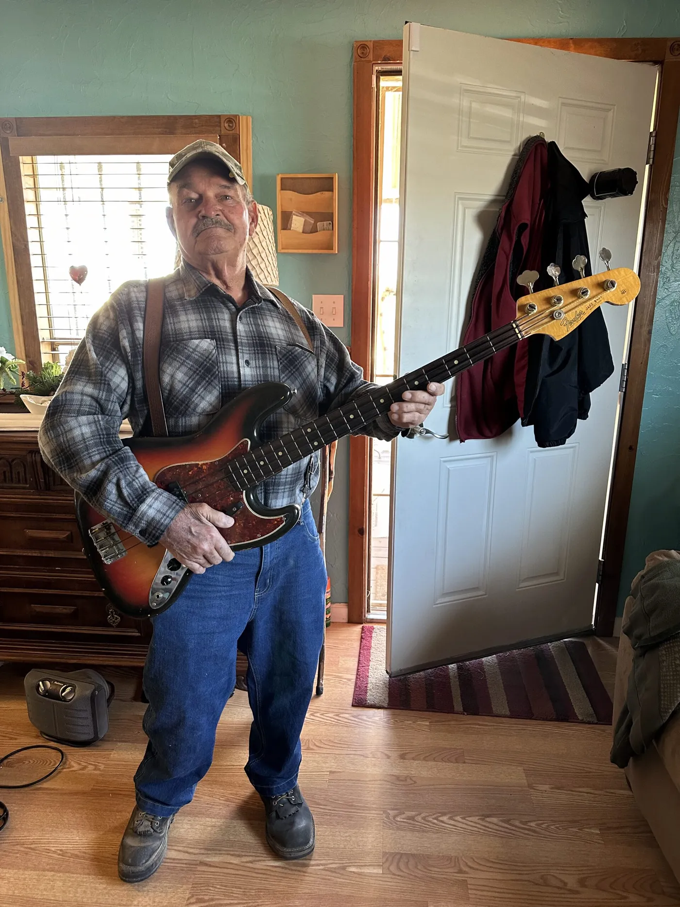 The original owner of a 1964 Fender Jazz Bass holding it, showing the sunburst body, tortoiseshell pickguard, unbound rosewood board with dot inlays, and the three knob chrome control plate
