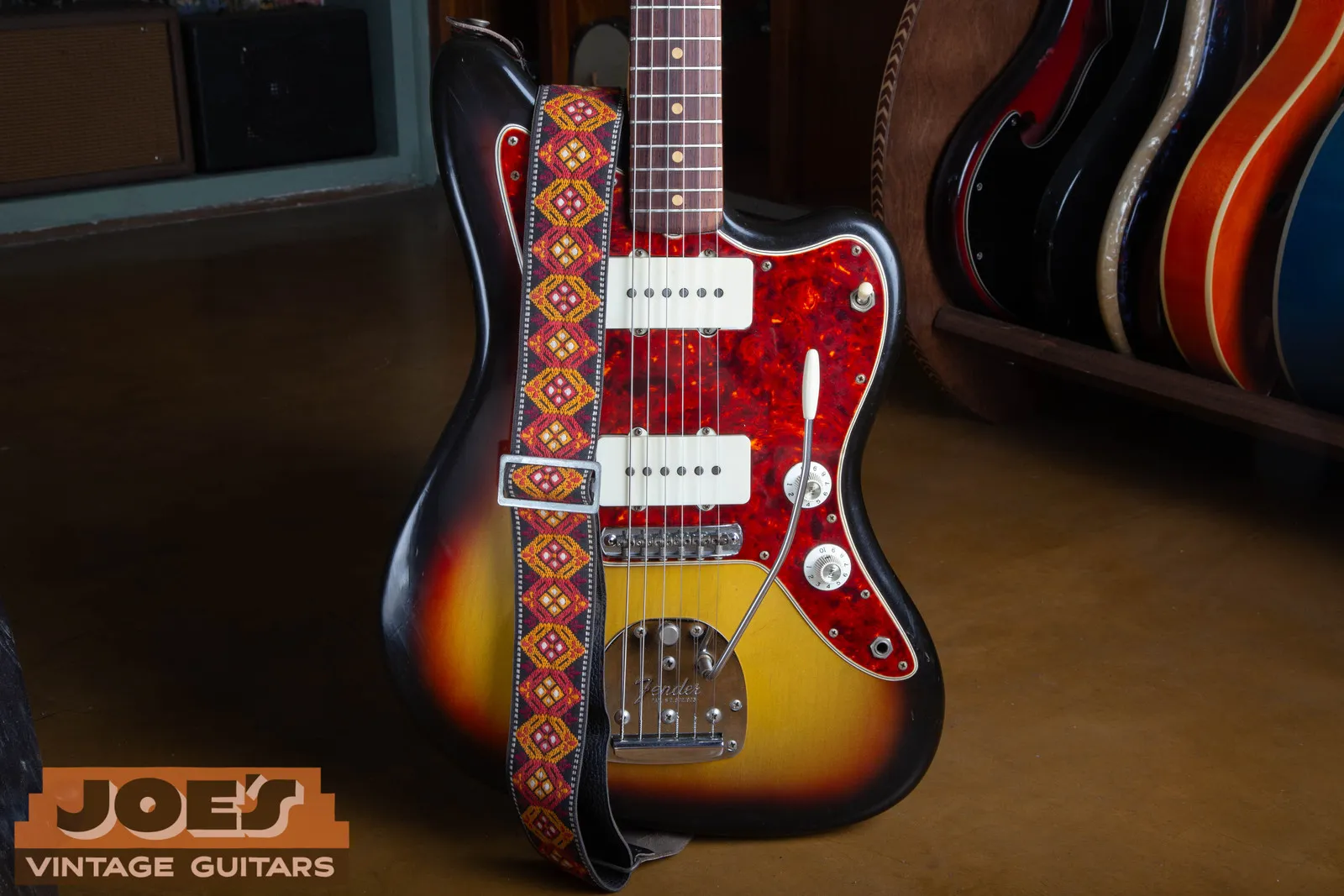 1965 Fender Jaguar in three-tone sunburst with a tortoise pickguard and a woven strap, in the shop.