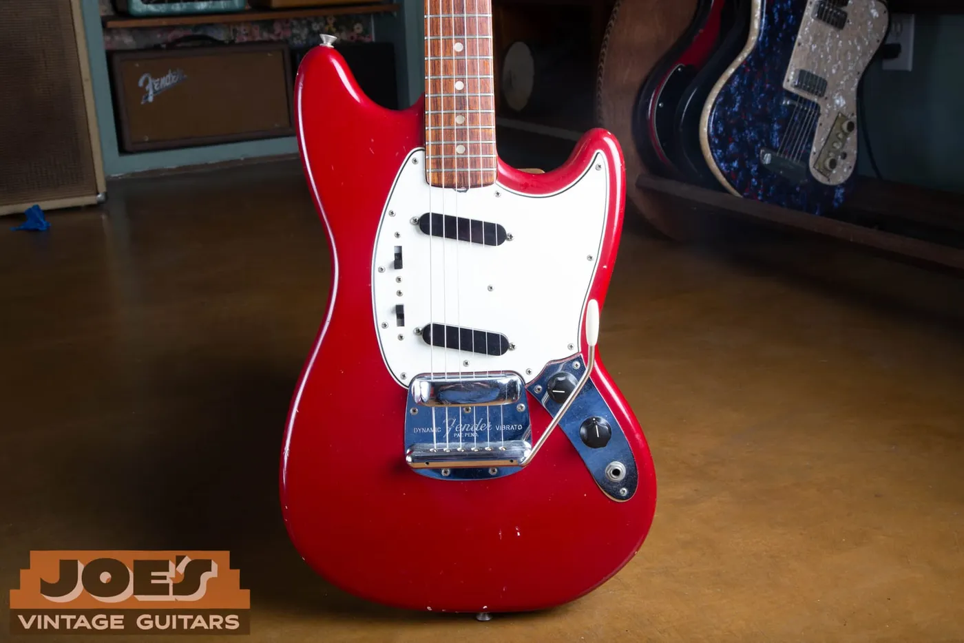 Front of a 1965 Fender Mustang in Dakota Red showing the two angled single-coil pickups, the two slide switches, the control plate and the Dynamic Vibrato
