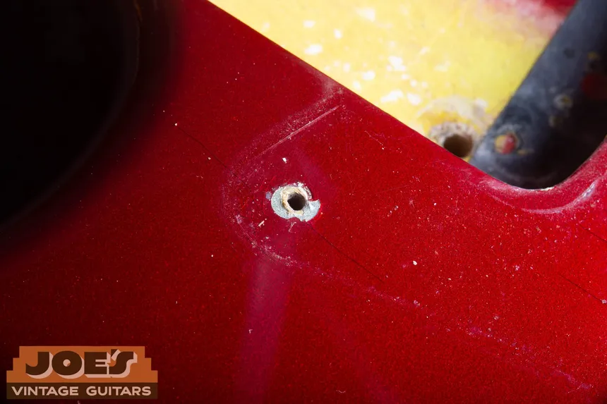 Close-up of a pickguard screw hole on a Candy Apple Red 1965 Stratocaster, with silver undercoat exposed at the chip.