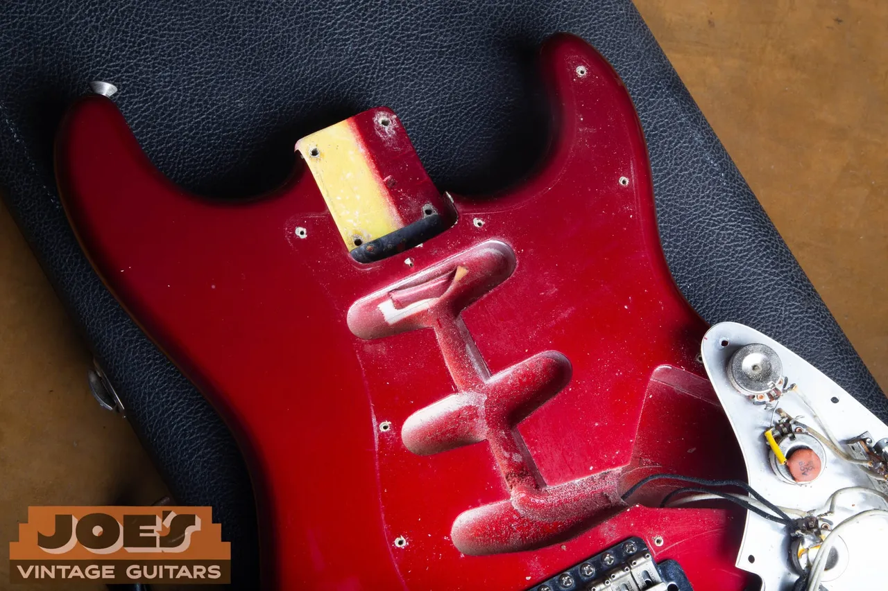 Red electric guitar body during inspection with dust visible around the exposed pickup cavities