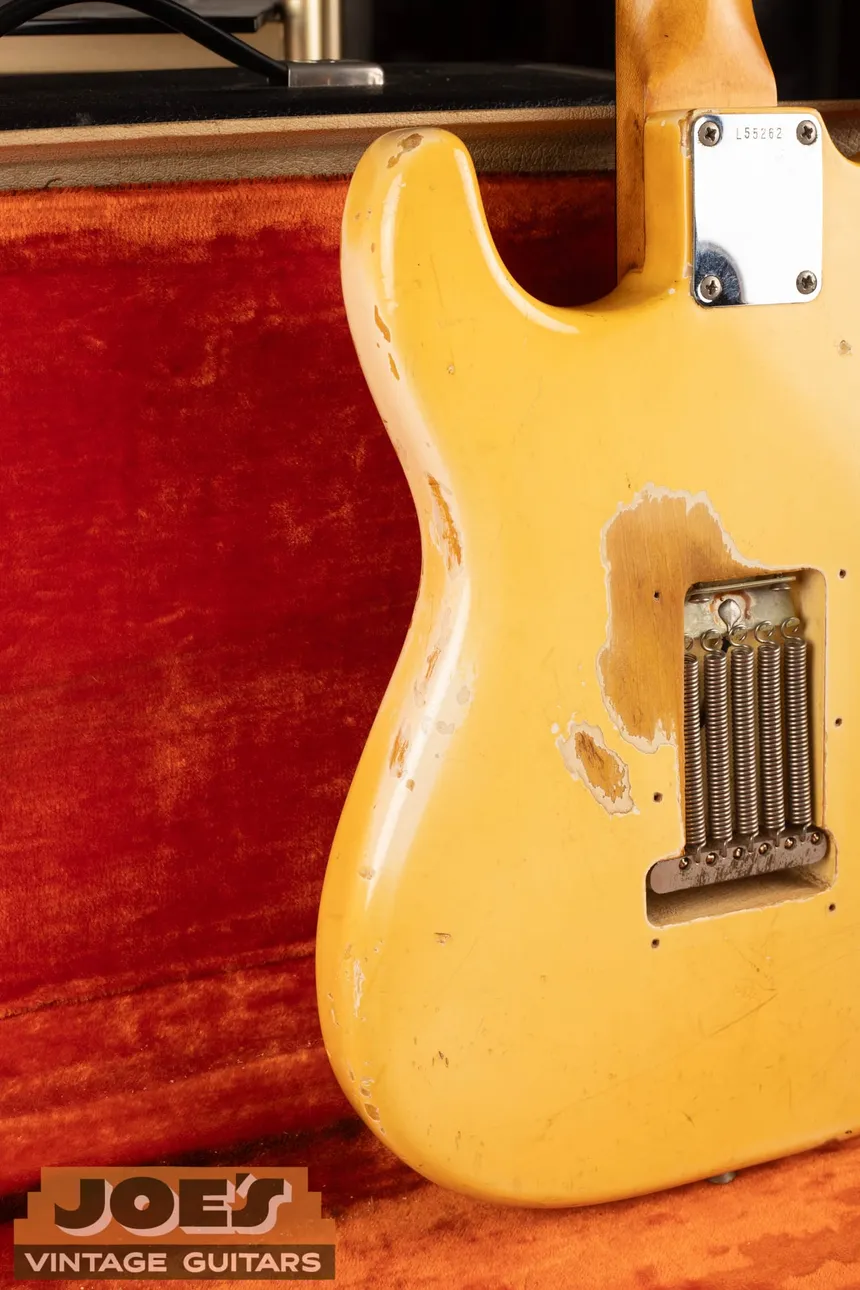 Back of an Olympic White 1965 Fender Stratocaster with ambered finish, worn wood and a whiter layer at the wear boundary.