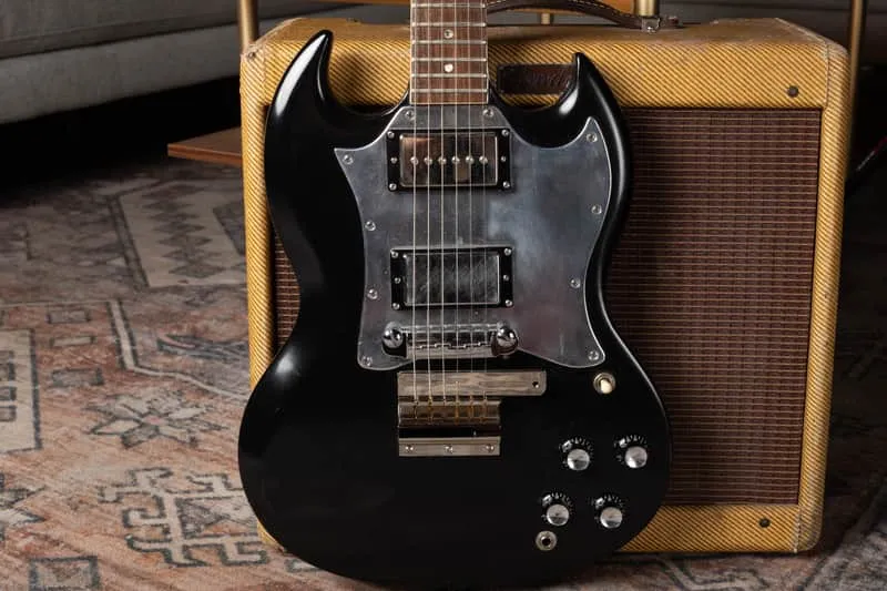 Black 1969 Gibson SG Special with replacement humbuckers and pickguard, photographed in front of a Fender amplifier.