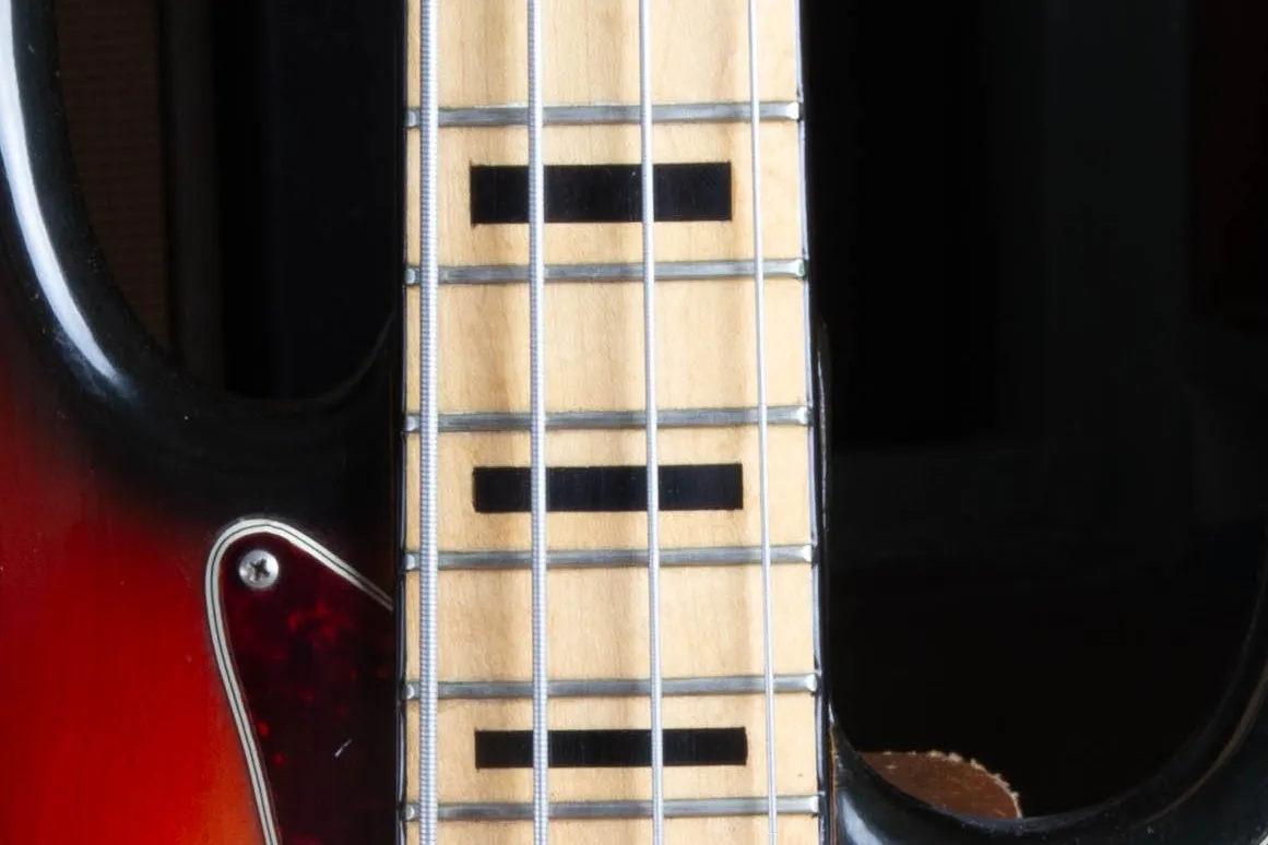 Close up of the maple fingerboard on a 1973 Fender Jazz Bass showing bold black block inlays and amber toned maple under the lacquer