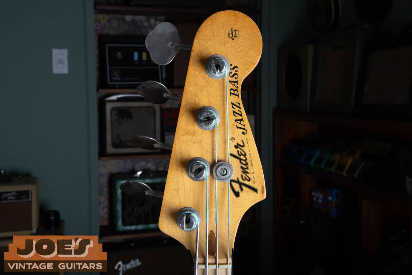The front of the headstock on a 1973 Fender Jazz Bass showing the thick black CBS logo reading Fender Jazz Bass, with a maple neck and four in line tuners