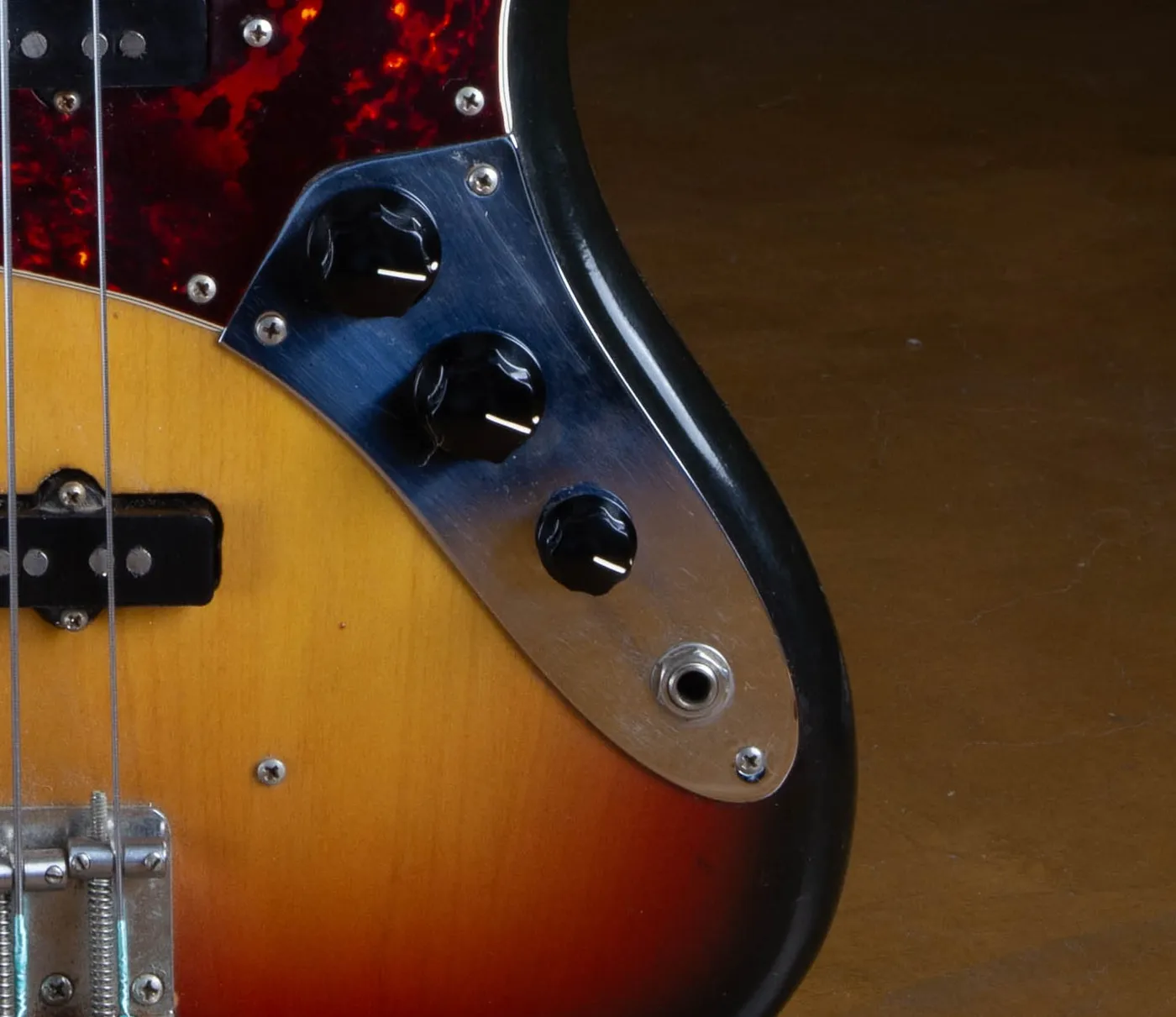 The chrome control plate of a 1973 Fender Jazz Bass with three separate black knobs and the output jack