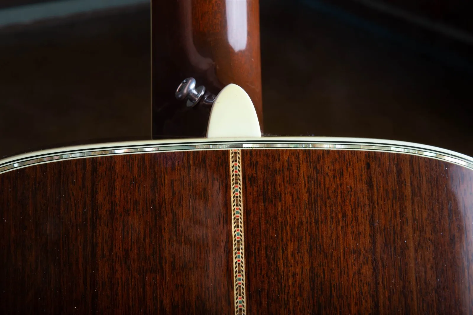 Close-up of the upper back and side of a 1976 Martin 000-45 showing abalone pearl inlay running along the back and side edges, the multi-color zipper backstrip, ivoroid binding, and the mahogany neck heel with a strap button.