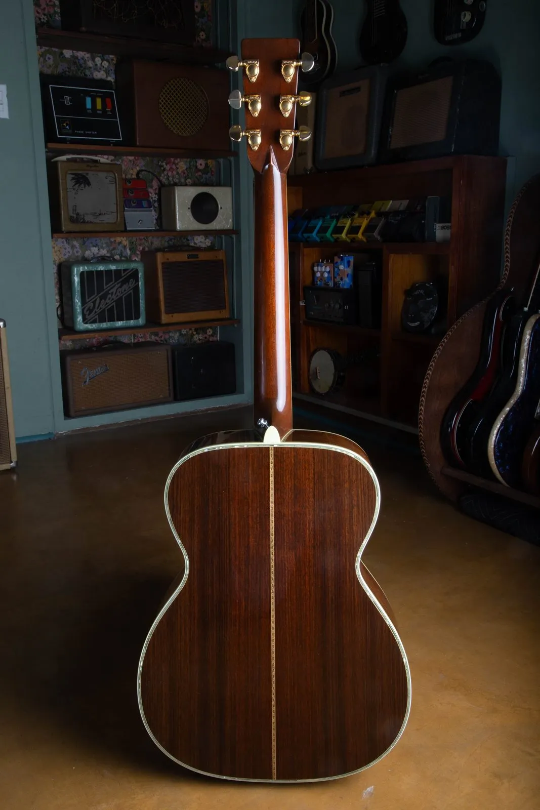 Full back view of a 1976 Martin 000-45 acoustic guitar standing upright, showing the mahogany neck, gold Grover tuners, and the abalone-bordered East Indian rosewood back.