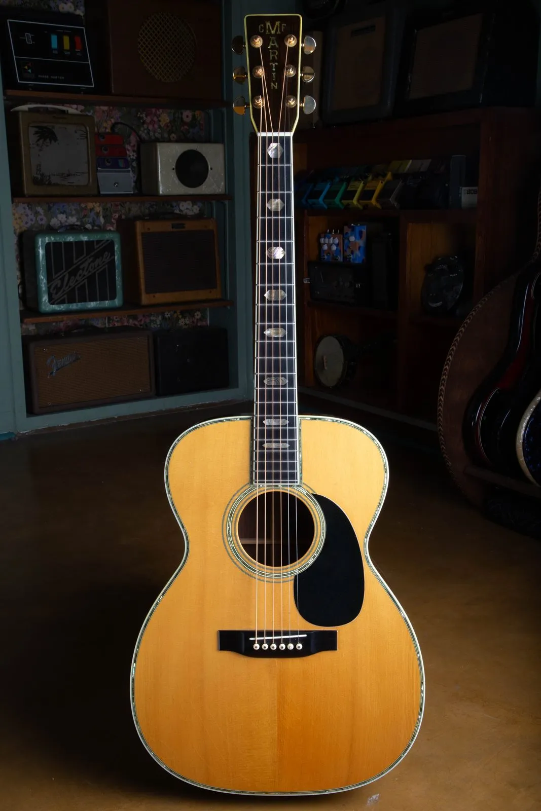 Full front view of a 1976 Martin 000-45 acoustic guitar standing upright in a vintage guitar shop, showing the natural spruce top, abalone trim, ebony fingerboard with hexagon inlays, and rosewood headstock.