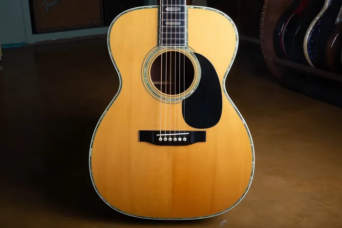Spruce top of a 1976 Martin 000-45 showing the abalone pearl border around the top edge and soundhole, black pickguard, and ebony belly bridge