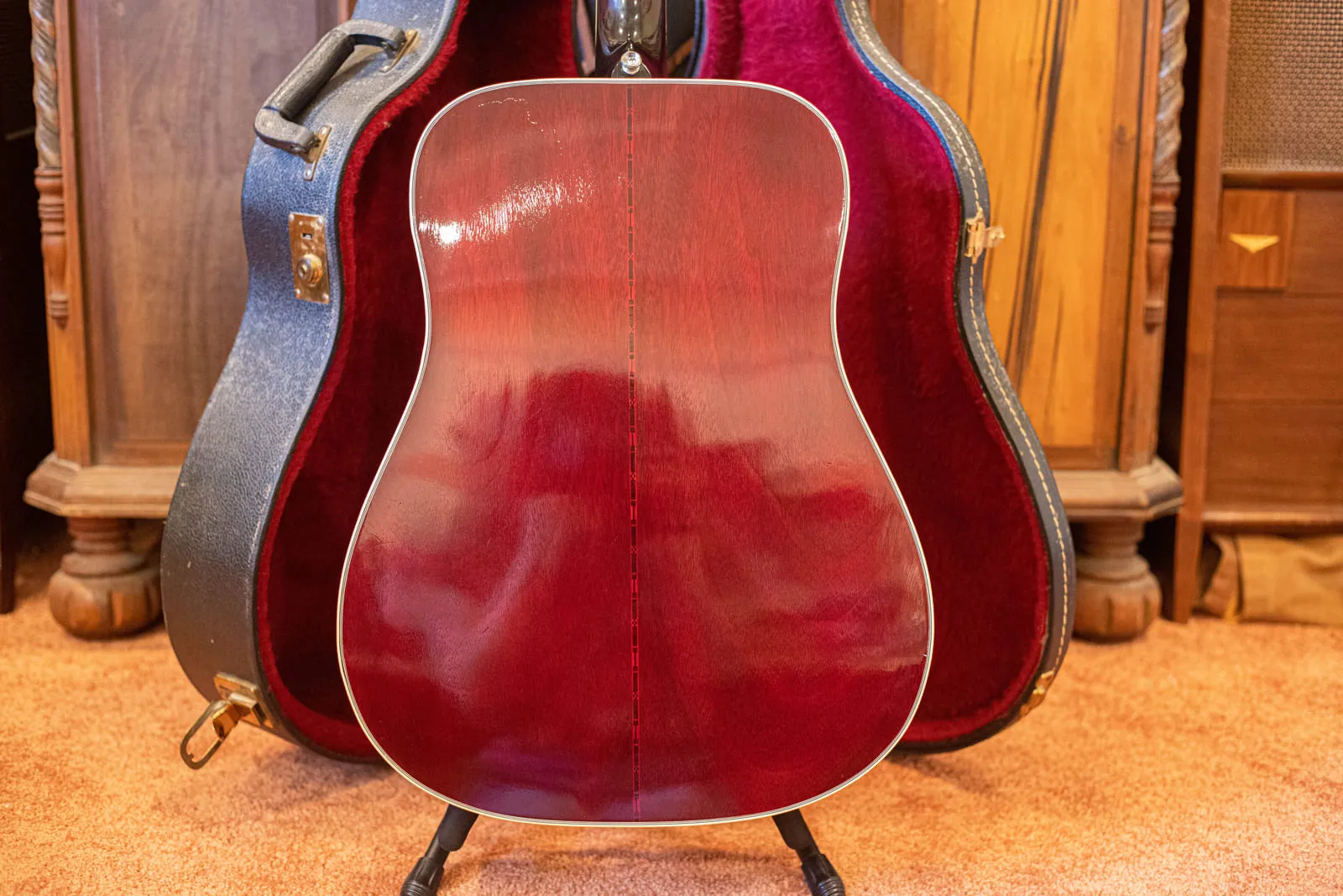 Back of a 1979 Gibson Hummingbird showing the dark cherry mahogany with a decorative marquetry center strip and light finish checking, sitting in a blue case with red plush lining.
