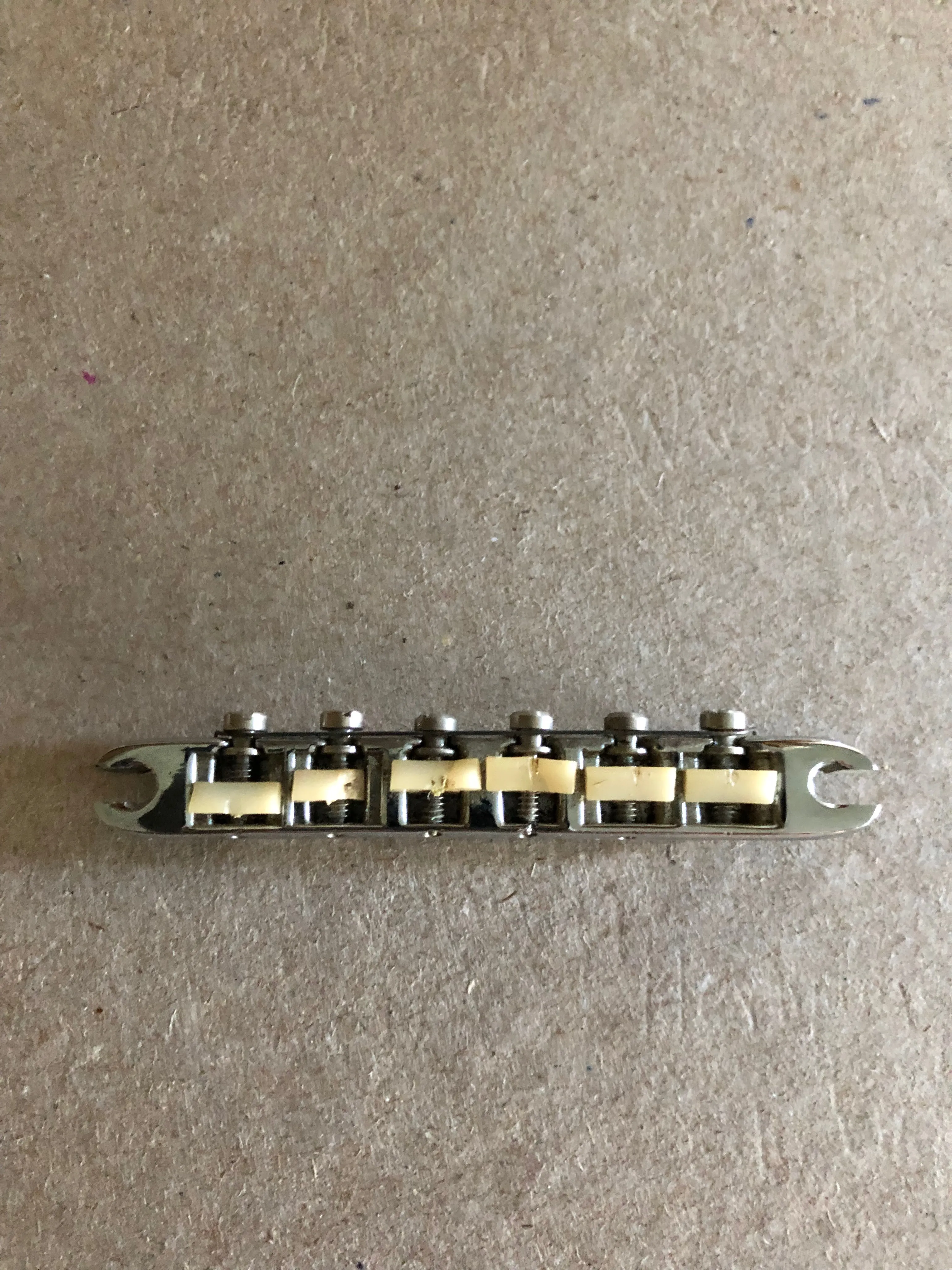 Detached Dove Tune-o-matic saddle assembly showing six light-colored saddles and adjustment screws