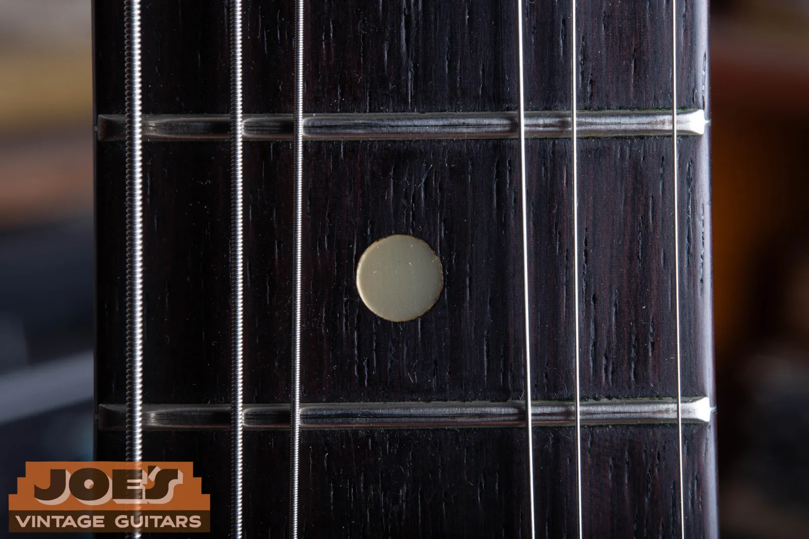 A pearloid dot inlay on a Fender Jazzmaster fingerboard, bright white and reflective