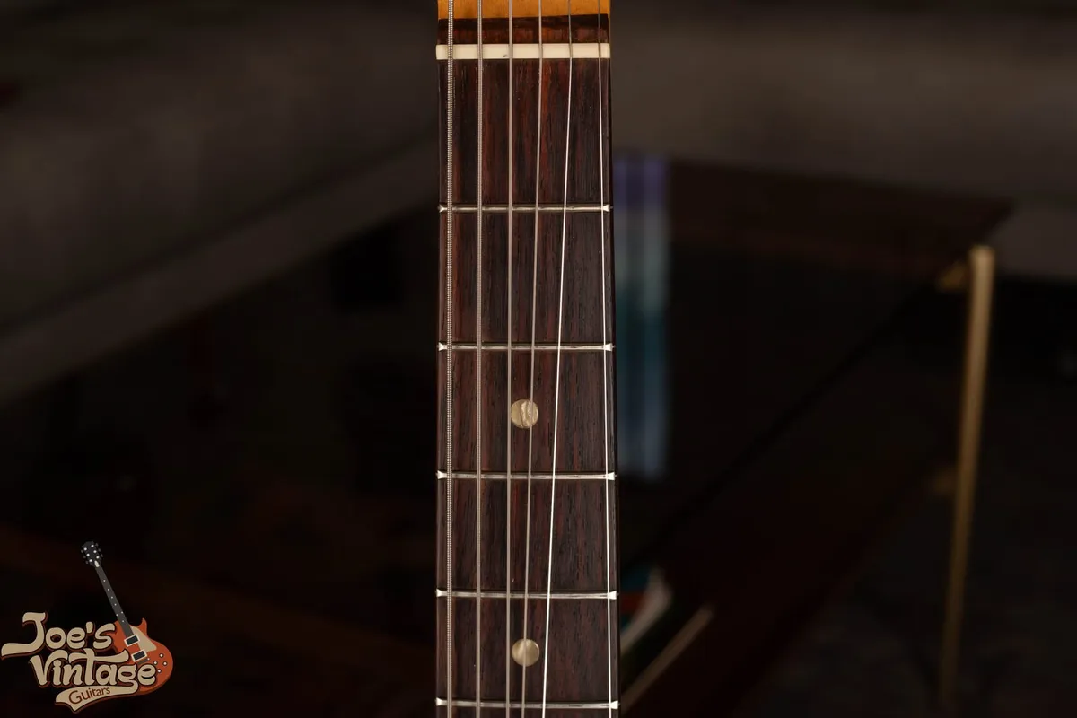 The rosewood fingerboard of a vintage Fender Mustang showing pearloid dot inlays on the veneer board