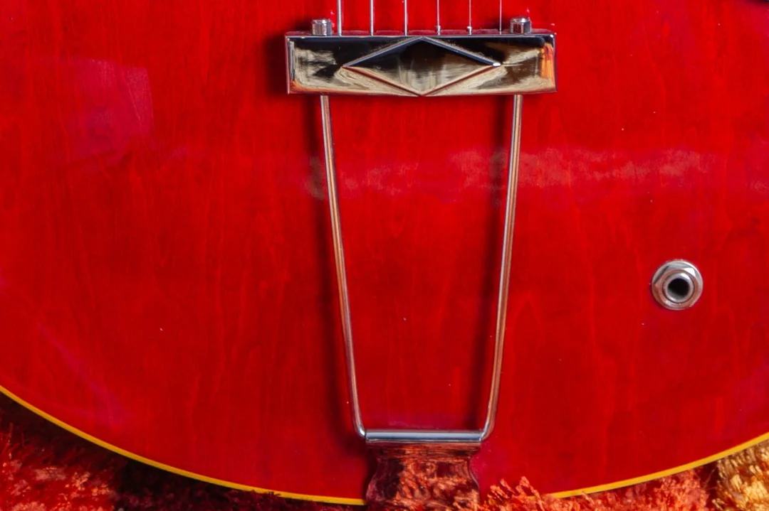 Chrome trapeze tailpiece mounted to the rim of a red Gibson semi-hollow guitar