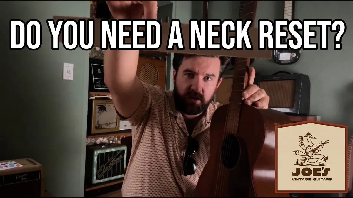 Joe Dampt holding a vintage mahogany flat-top guitar with a flat straightedge laid along the fretboard and pointed at the bridge, checking the neck angle.
