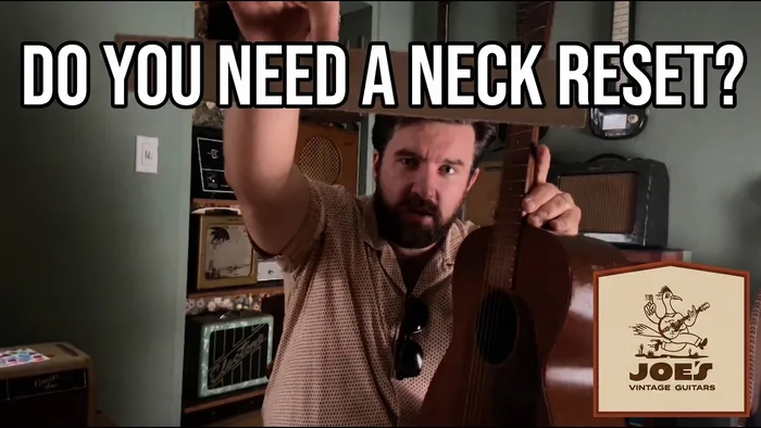 Joe Dampt holding a vintage mahogany flat-top guitar with a flat straightedge laid along the fretboard and pointed at the bridge, checking the neck angle.
