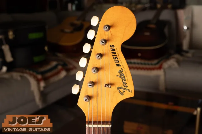 Headstock of a vintage Fender Mustang showing the gold transition Fender logo above the Mustang model name on a maple face