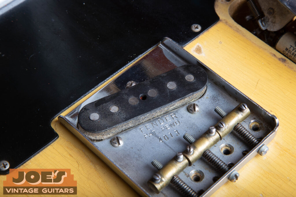 Alt TextClose-up of an original 1952 Fender Telecaster bridge pickup featuring flat pole pieces and black string wrapping