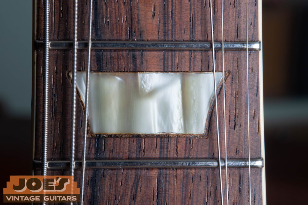 Macro shot of a 1956 Gibson Les Paul fretboard showing a Cellulose Nitrate trapezoid inlay with a marbled texture and sharp corners set in Brazilian Rosewood.