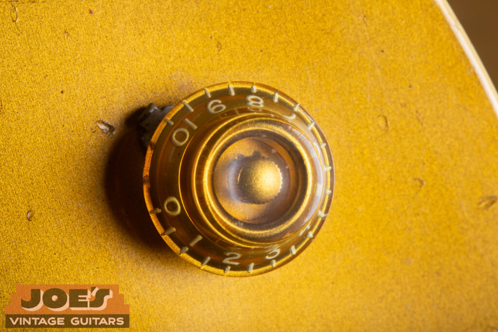 Alt TextMacro close-up of a 1956 Gibson Les Paul gold "Top Hat" control knob and a sharp nickel "finger bleeder" pointer washer on an original bullion gold finish.