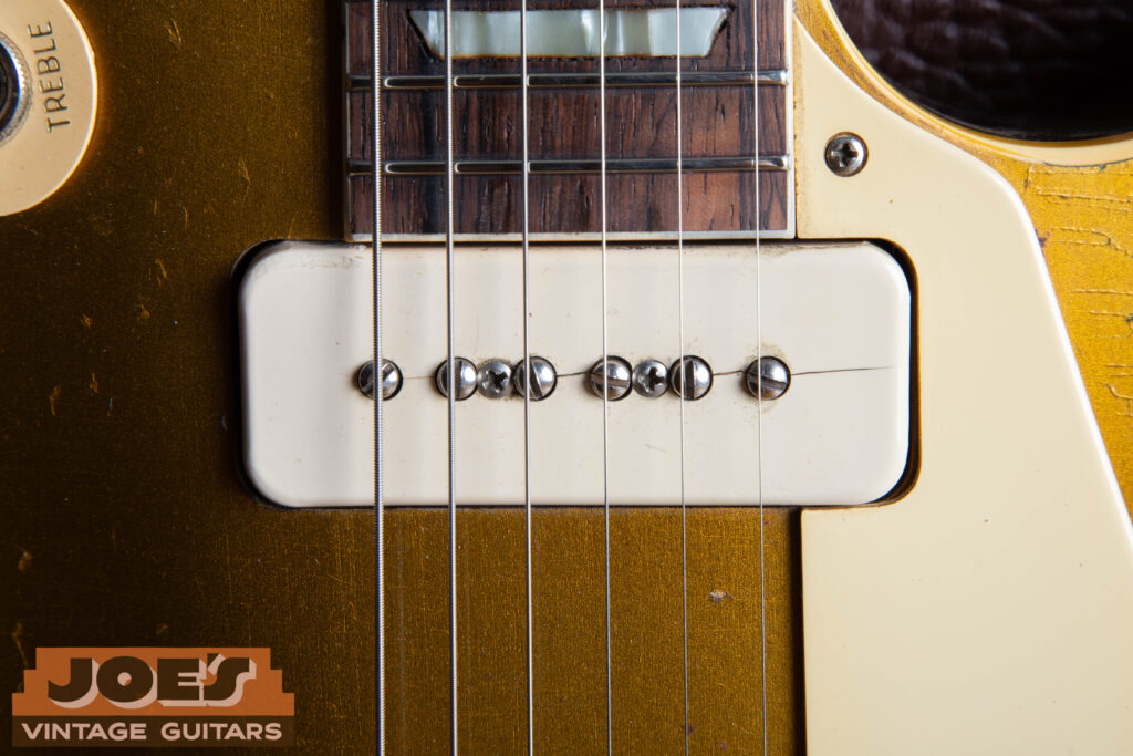 Macro close-up of a 1956 Gibson Les Paul neck P-90 pickup showing a cream Royalite soapbar cover with a vintage hairline split running along the center of the pole pieces.