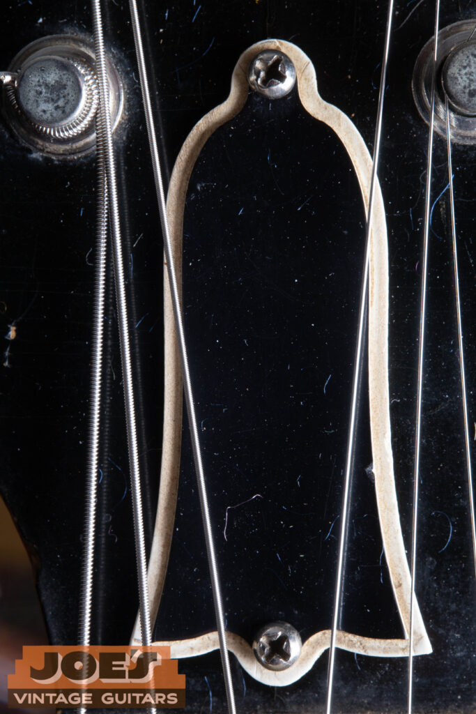 Macro close-up of a 1956 Gibson Les Paul truss rod cover, showing the period-correct two-ply black and white bell-shaped plastic and the original mounting screws.