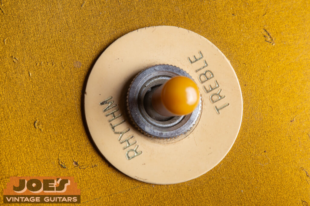 Close-up of a 1956 Gibson Les Paul 3-way toggle switch featuring an aged amber Catalin tip and a cream "poker chip" selector ring with gold-embossed lettering.