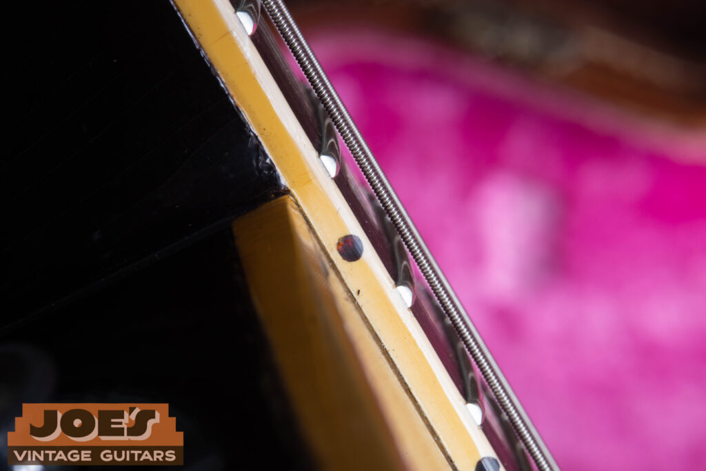 Macro close-up of a 1957 Gibson Les Paul neck binding, showing the original dark reddish tortoise shell side dot inlays with a subtle marbled texture.