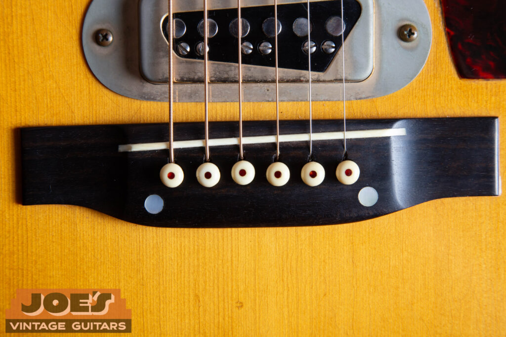 Close-up of a 1959 Martin D-28E ebony bridge featuring two pearl dots hiding the factory-installed bolts and an original bone saddle.